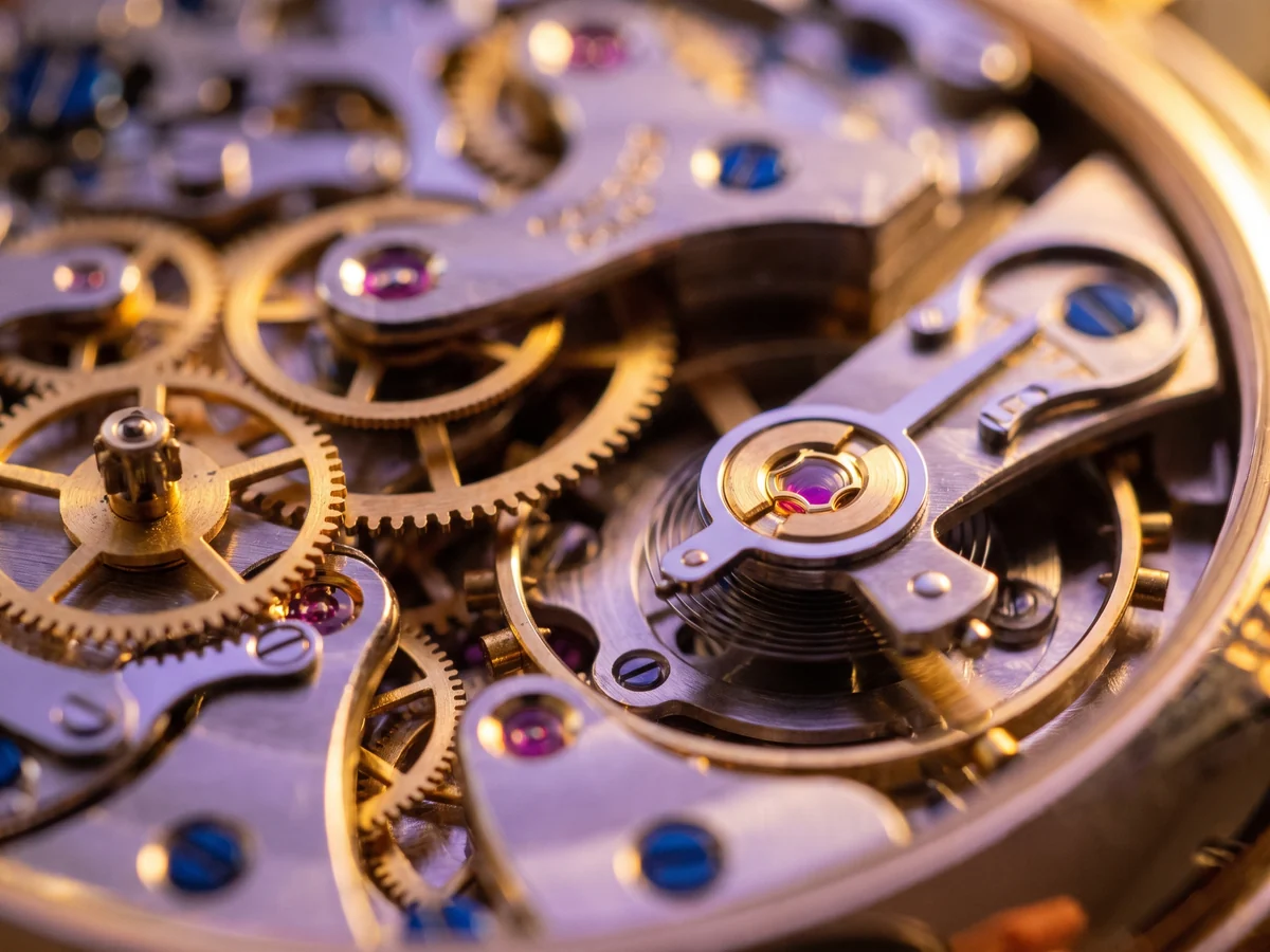 Macro view of a fine mechanical watch movement, brass gears meshing and a ruby jewel catching the light, a metaphor for business processes that run themselves