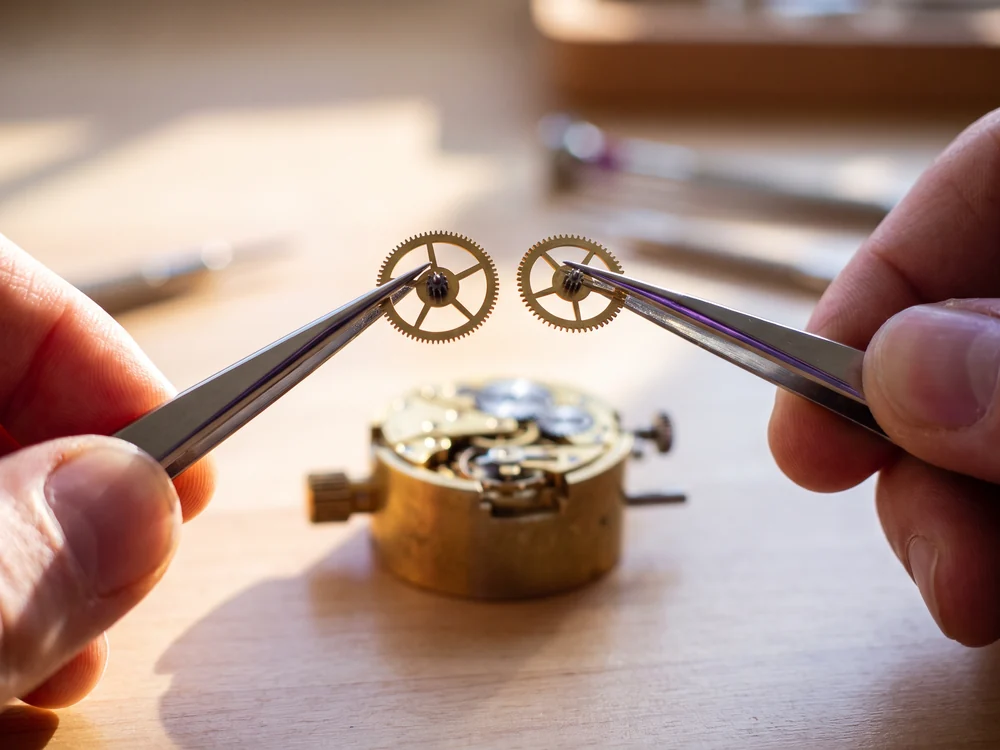 A watchmaker holding two different gear wheels side by side in tweezers to choose the right one, a metaphor for designing the automation