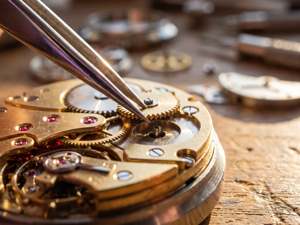 Fine tweezers lowering a brass gear precisely into a part-assembled movement so its teeth mesh, a metaphor for building each automation rule