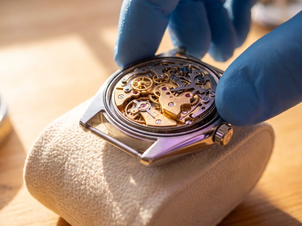 Gloved fingertips lowering a completed movement into its polished case, a metaphor for a clean cutover into production