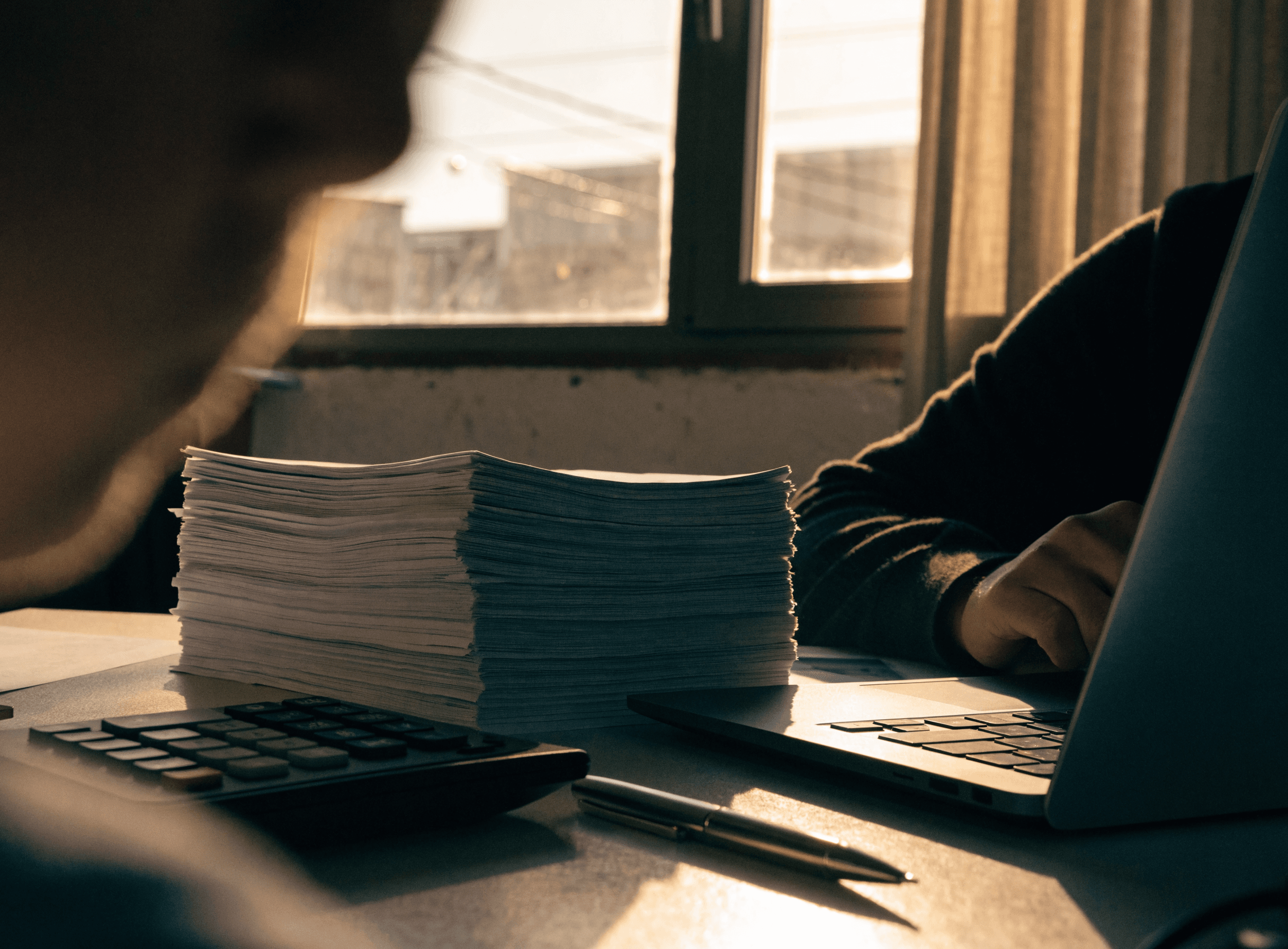 Stacked freight invoices, a calculator and a laptop on a settlement desk