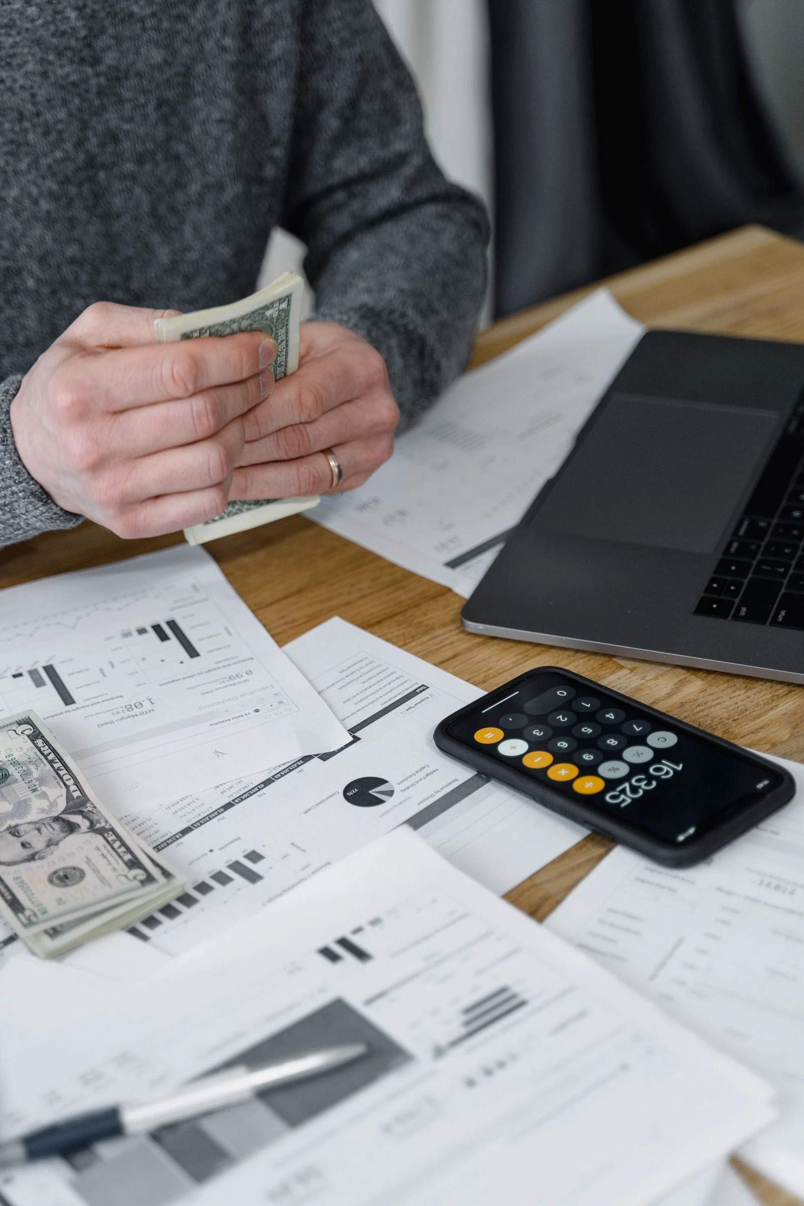 Hands counting cash with payroll spreadsheets and a calculator