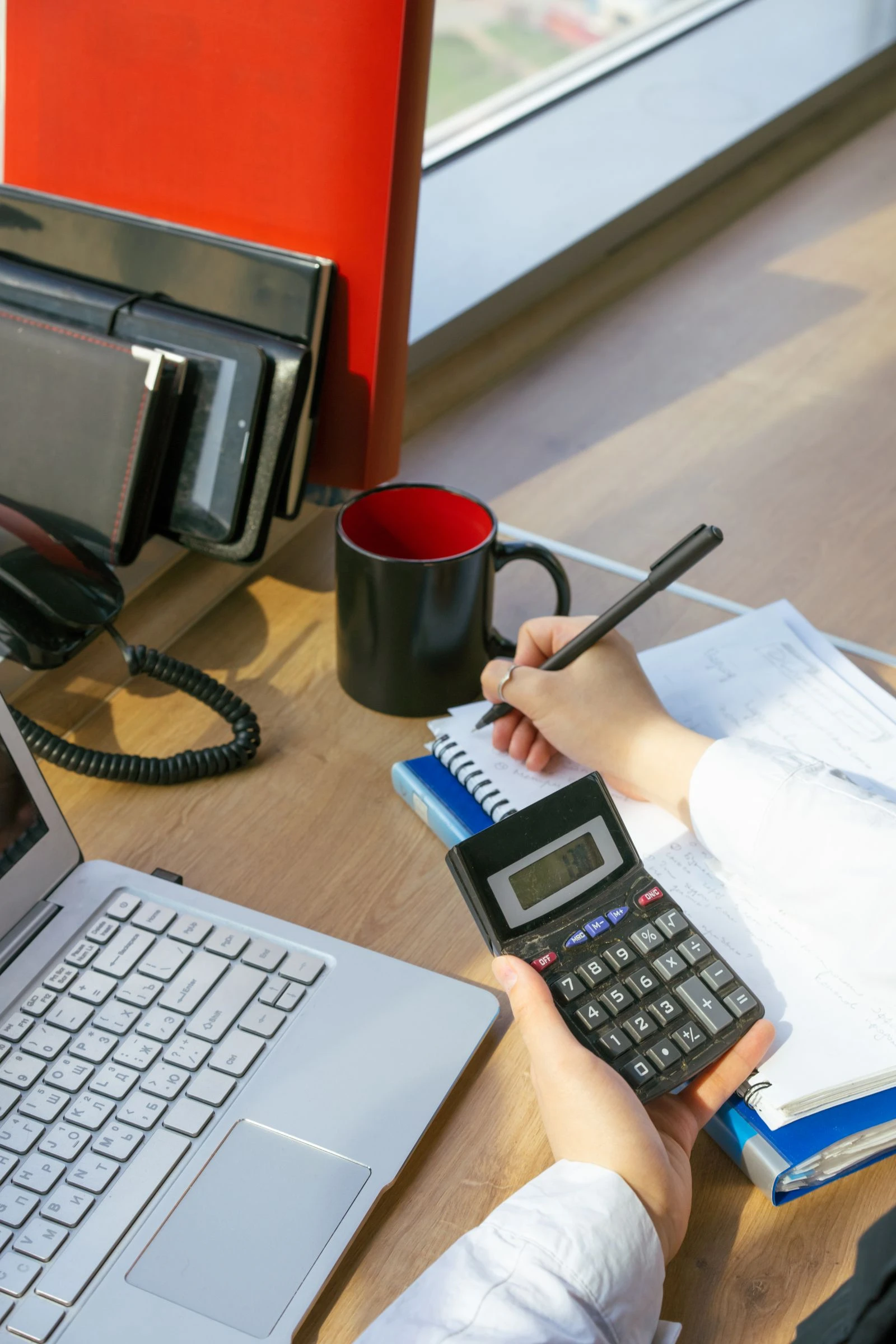 Person writing pay figures in a notebook with a calculator